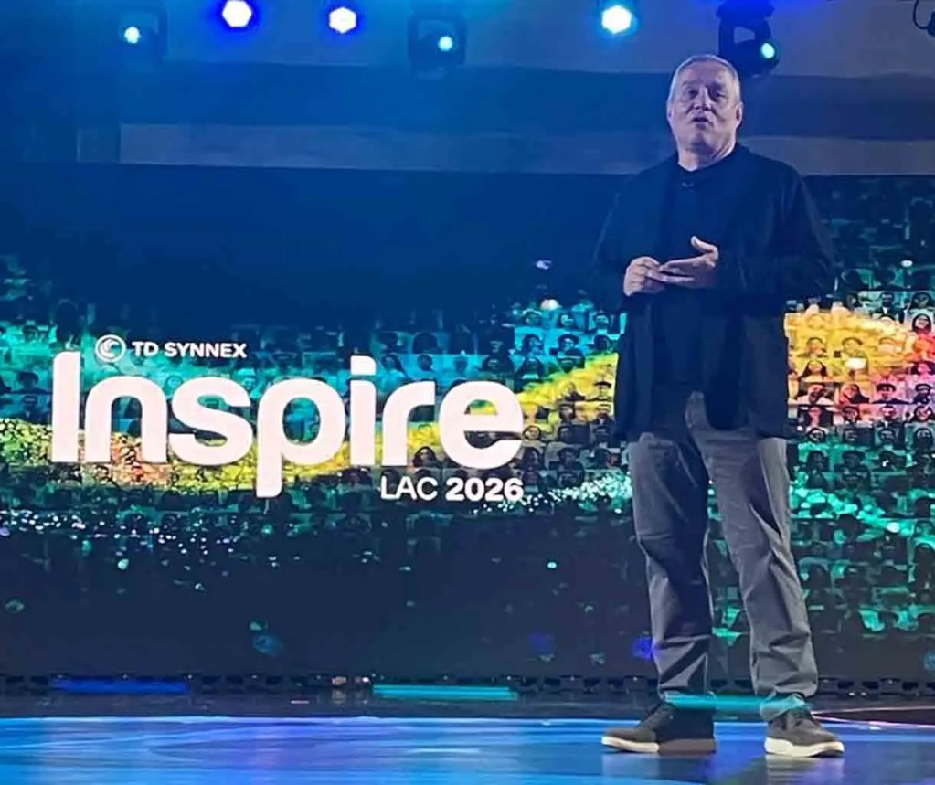 Un hombre de pie en un escenario presentando en el evento Inspire LAC 2026, con un fondo colorido que muestra imágenes de personas.