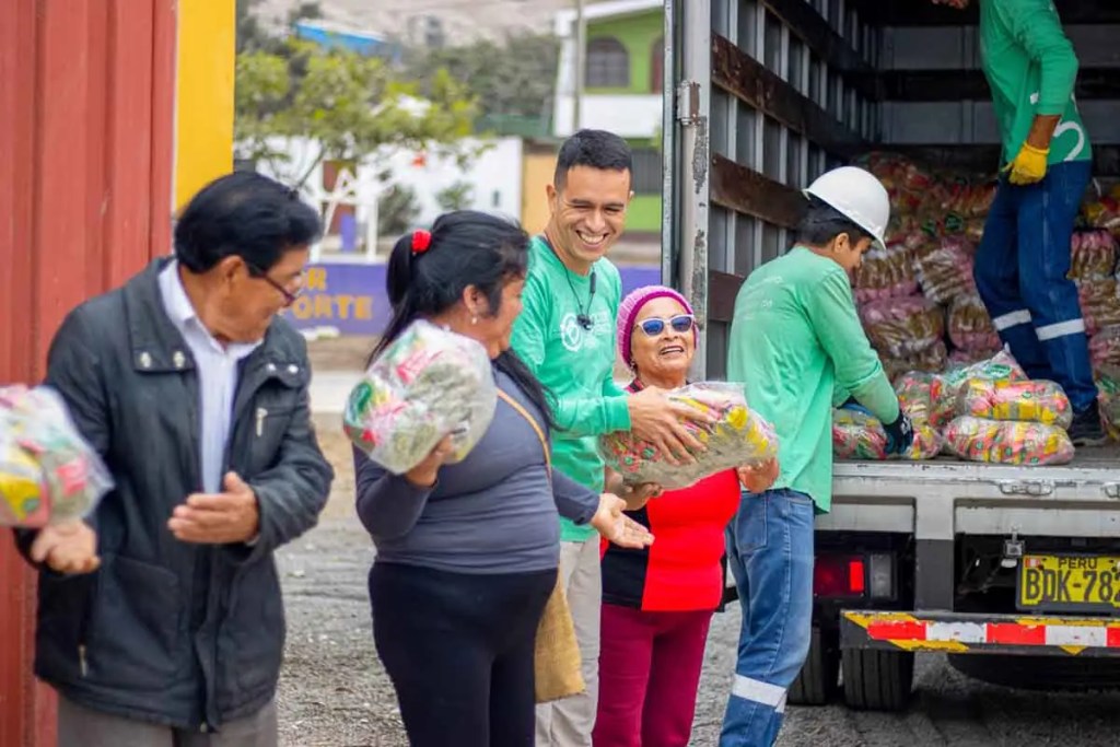 Grupo de personas sonriendo y sosteniendo paquetes de alimentos durante una entrega comunitaria.