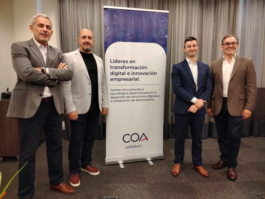 Cuatro hombres posando frente a un cartel que dice 'Líderes en transformación digital e innovación empresarial'.