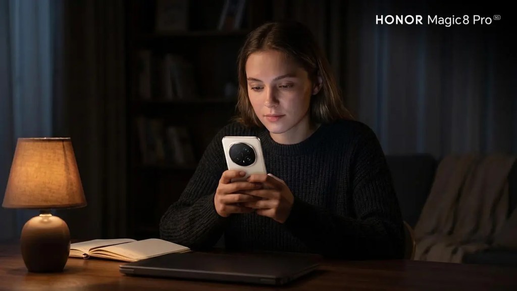 Una mujer sentada en una mesa oscura, usando un teléfono móvil, con una lámpara encendida y un cuaderno a su lado.