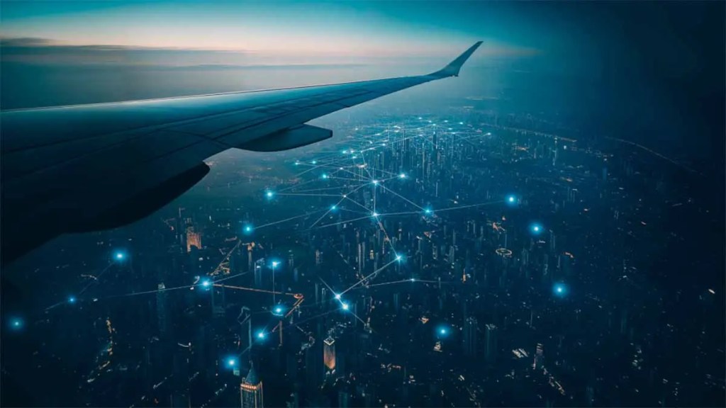 Vista aérea de una ciudad iluminada por la noche desde la ventana de un avión, con un ala visible en primer plano y líneas de conexión brillantes que sugieren una red urbana.