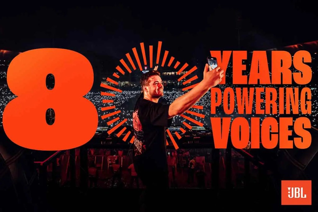 Un hombre sonriendo mientras sostiene un teléfono en un concierto, con el texto '8 AÑOS POTENCIANDO VOCES' en letras grandes y vibrantes.