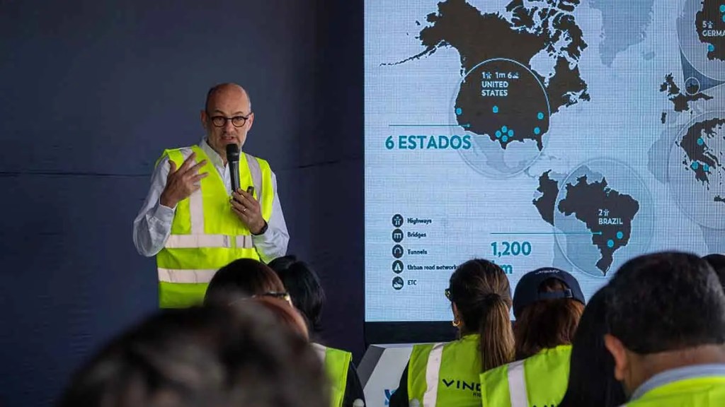 Presentación de un orador con chaleco reflectante en un evento, explicando un mapa que muestra información sobre Estados Unidos y Brasil.
