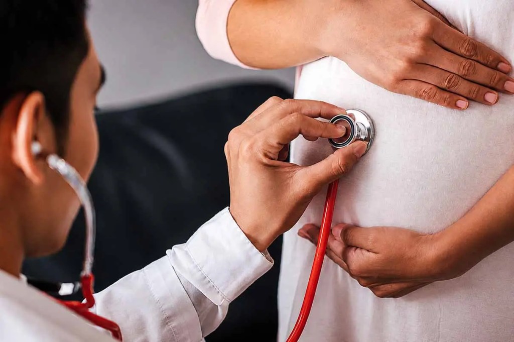 Médico usando un estetoscopio en el abdomen de una mujer embarazada.