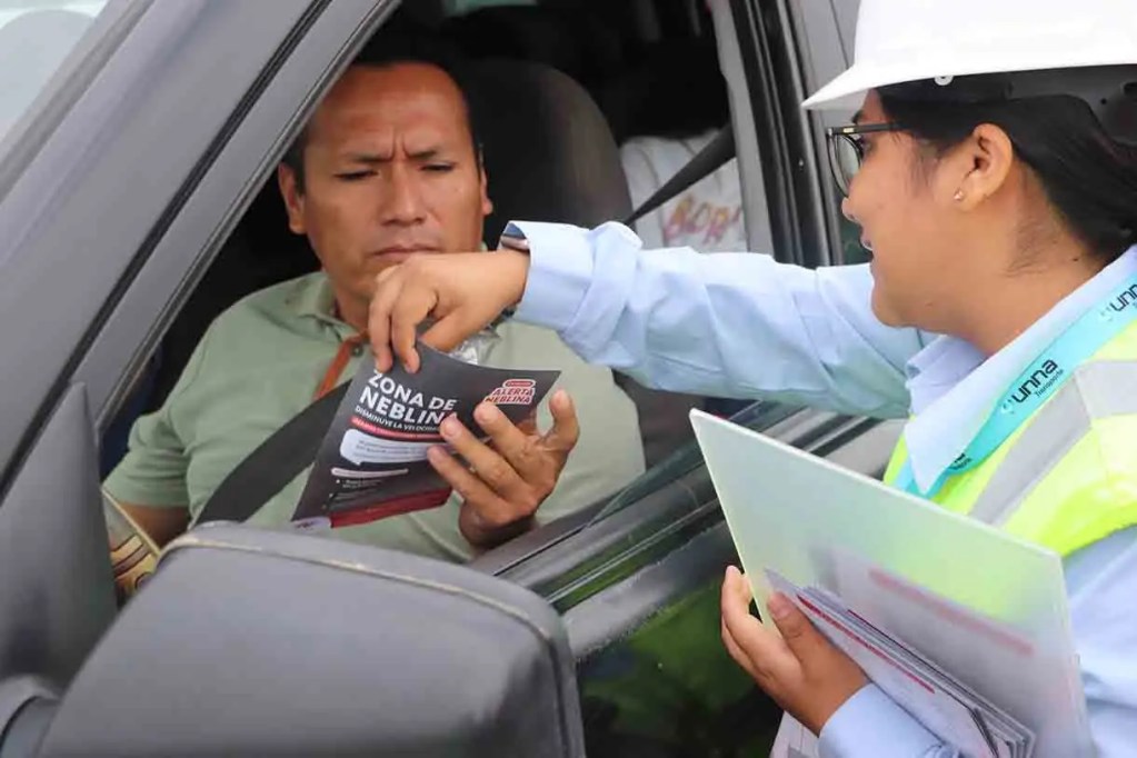 Una mujer entrega un folleto a un hombre dentro de un automóvil en un punto de control.