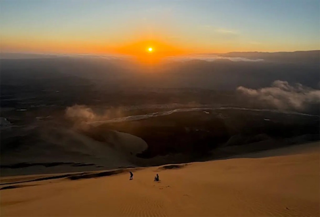 Atardecer sobre dunas de arena con dos personas en la parte inferior