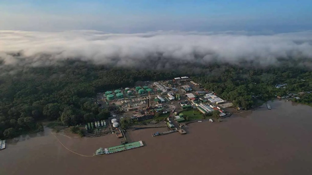 Vista aérea de una planta industrial junto a un río, con nubes bajas y vegetación densa alrededor.