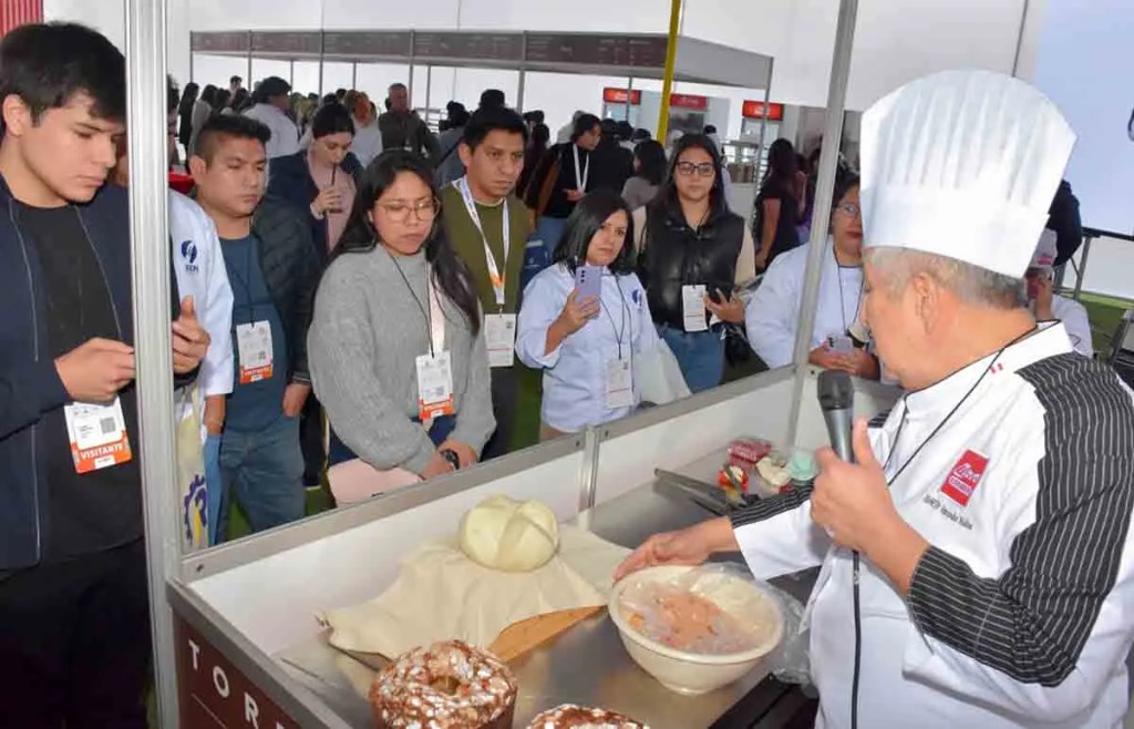Un chef presenta una demostración de cocina a un grupo de personas interesadas, mostrando ingredientes y técnicas de preparación.