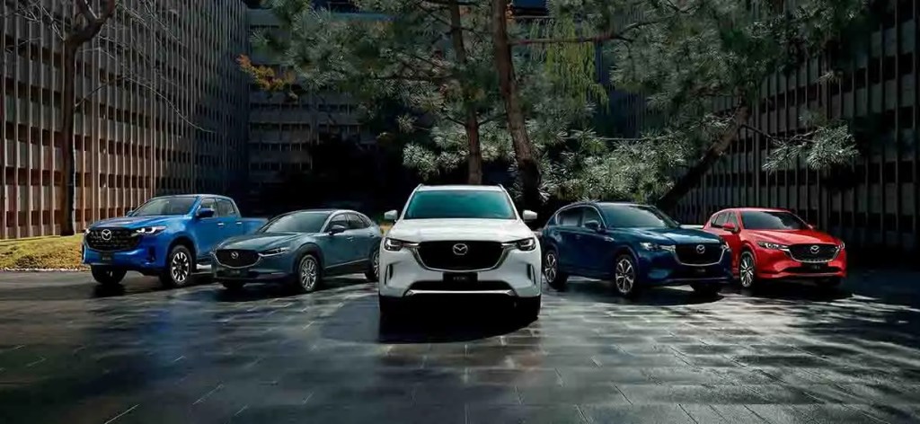 Cinco vehículos de la marca Mazda en una exhibición al aire libre, con un fondo de edificios y árboles.