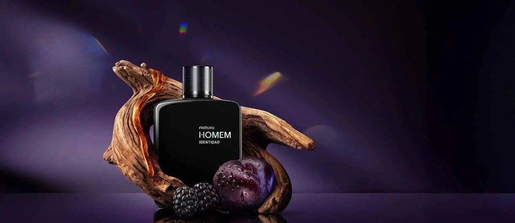 Frasco de perfume negro de Natura HOMEM con maderas y frutas en una presentación estilizada sobre un fondo oscuro.