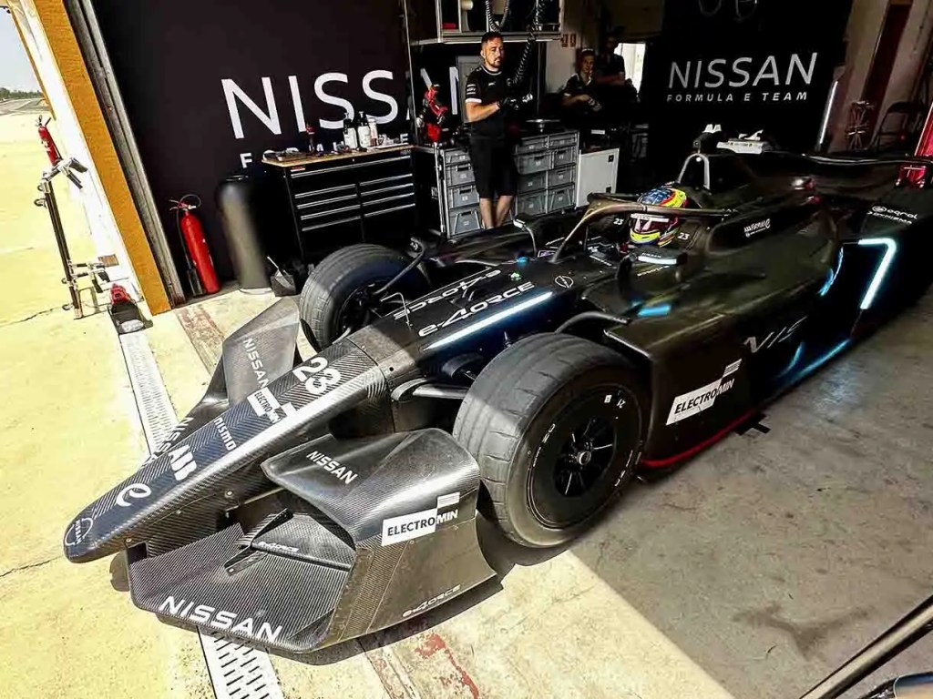 Coche de carreras de Fórmula E de Nissan en el garaje, con mecánicos trabajando en el fondo.
