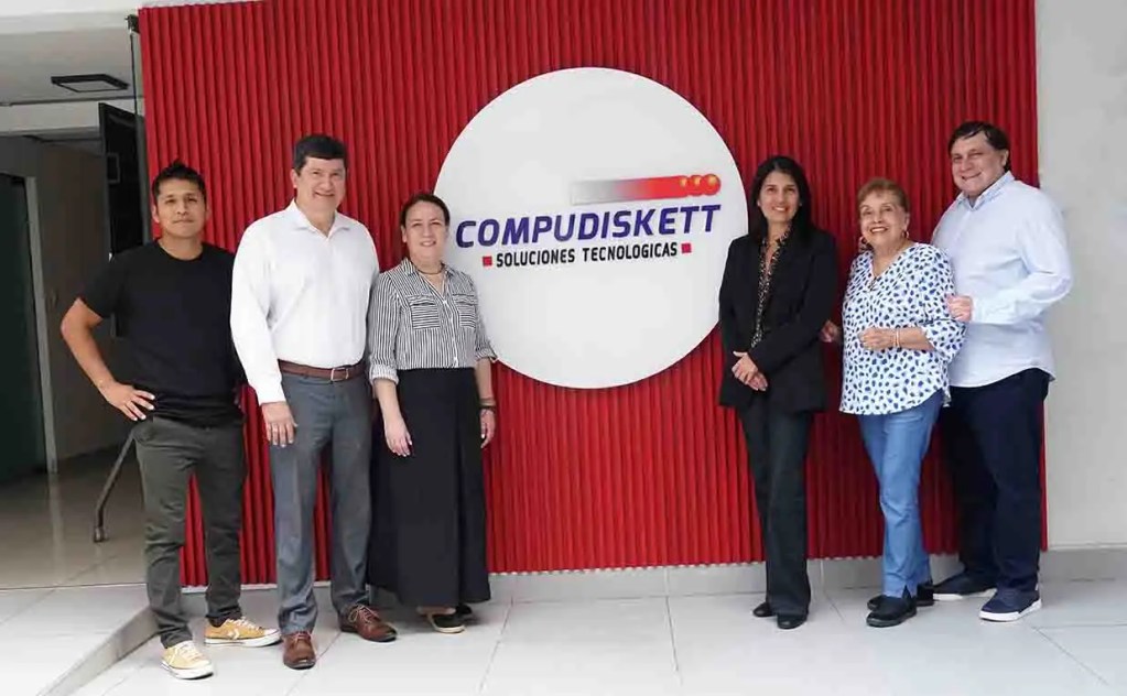 Grupo de seis personas posando frente a un muro con el logotipo de Compudiskett, una empresa de soluciones tecnológicas.