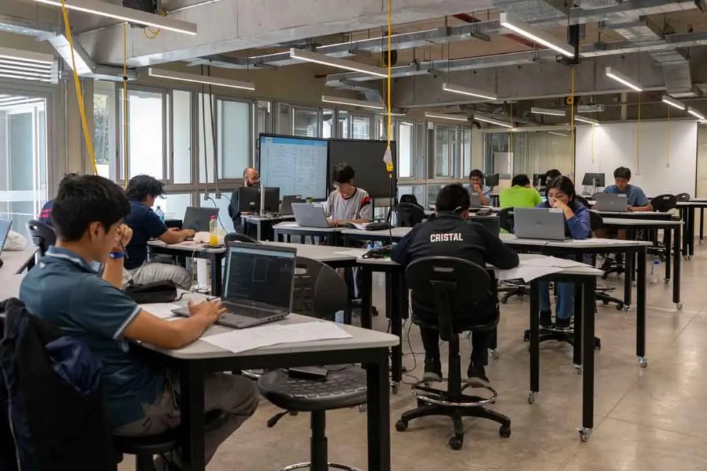 Estudiantes trabajando en un espacio de estudio moderno, utilizando computadoras portátiles en mesas.